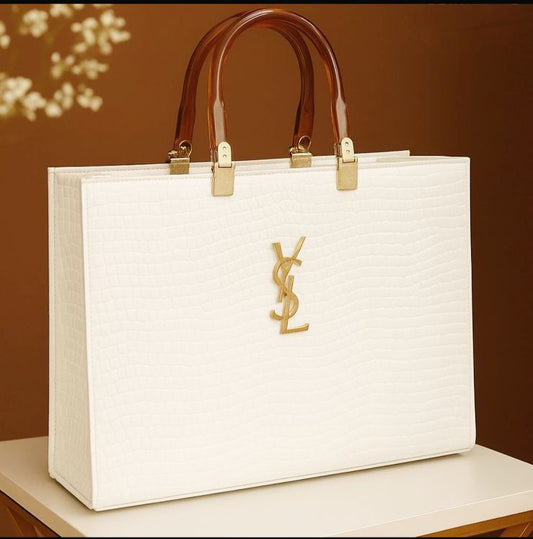 White handbag with brown handles on a white surface against a brown background